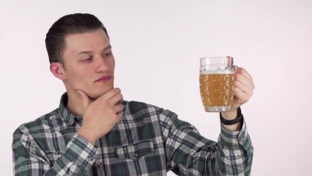 Jovem esfregando seu queixo pensativo, examinando cerveja em uma caneca — Vídeo de Stock