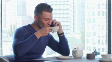 Yakışıklı adam çay içme ve restoranda telefonda konuşurken zevk