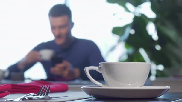 Kopje koffie of thee op de tafel, man genieten van ontbijt op de achtergrond — Stockvideo