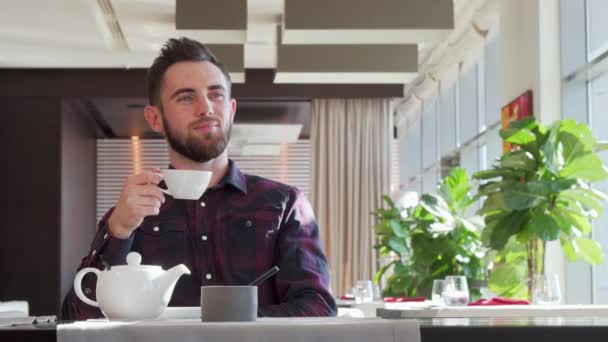 Hombre guapo barbudo mirando hacia otro lado pensativamente, disfrutando del té de la mañana — Vídeos de Stock