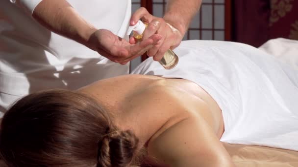 Professionele masseur olie toe te passen op de achterkant van zijn cliënt, voorbereiden om te masseren — Stockvideo