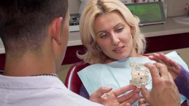 Приваблива зріла жінка розмовляє з стоматологом в його офісі — стокове відео