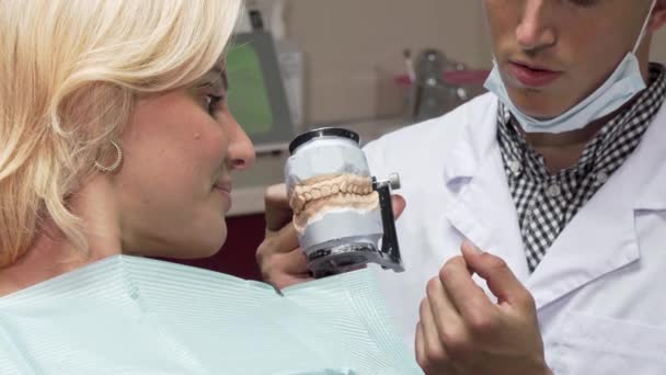 Мужчина-дантист, работающий в своей клинике, показывает пациенту зубную плесень — стоковое видео