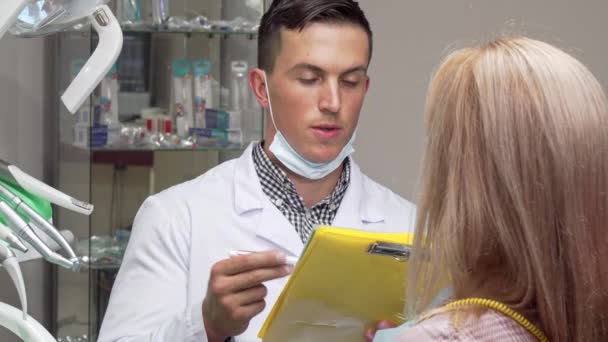 Young male dentist talking to his female patient, examining medical papers — Stock Video