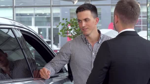 Hombre guapo estrechando la mano con vendedor de coches en la concesionaria de automóviles — Vídeo de stock