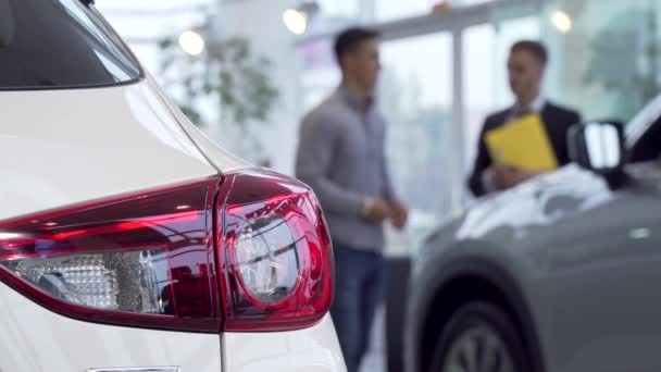 Luces de coche en primer plano, hombre comprando coche en el concesionario en el fondo — Vídeos de Stock