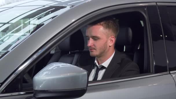Alegre hombre de negocios sosteniendo las llaves del coche sentado en un nuevo auto en el concesionario — Vídeos de Stock