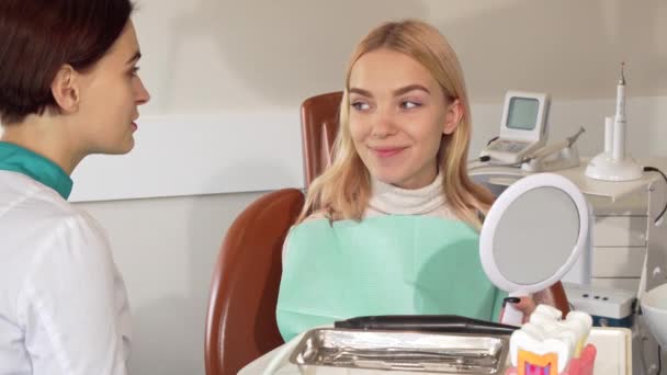 Mulher bonita feliz examinando seus dentes no espelho na clínica odontológica — Vídeo de Stock