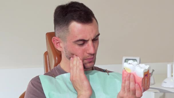 Jovem com dor de dente, sentado em uma cadeira dentária na clínica — Vídeo de Stock