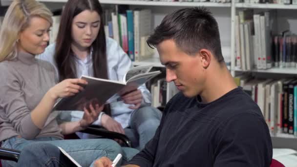 Guapo estudiante masculino sonriendo a la cámara, mientras hace los deberes en la biblioteca — Vídeos de Stock