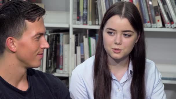 Atractiva joven mujer hablando con su amiga de la universidad en la biblioteca — Vídeos de Stock