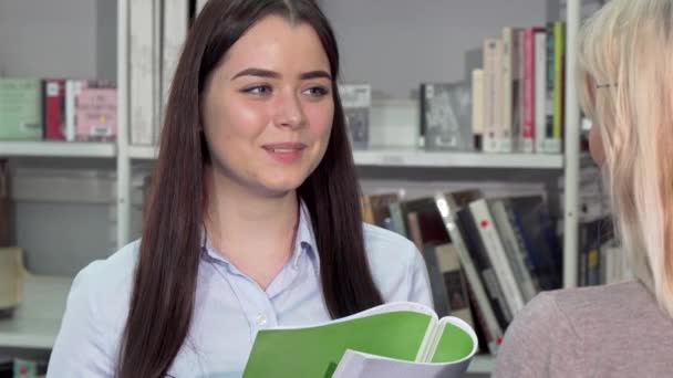 Mooie jonge vrouw lachen, praten met haar vriend op college library — Stockvideo