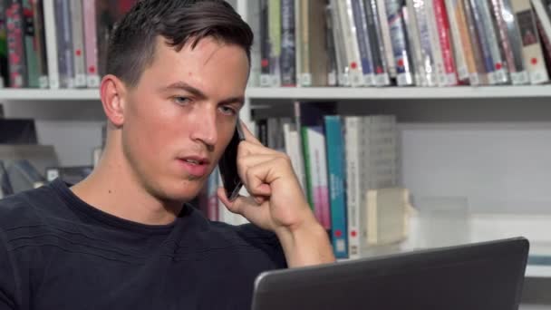 Handsome man talking on the phone, while doing homework on laptop — Stock Video