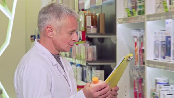 Старший фармацевт работает, читает газеты и изучает лекарства — стоковое видео