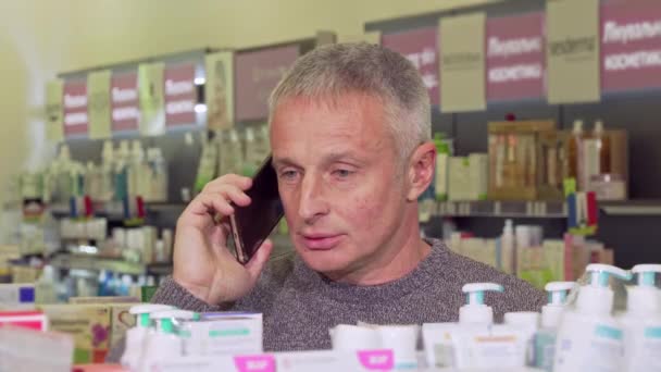 Senior man talking on the phone, while shopping at the pharmacy — Stock Video