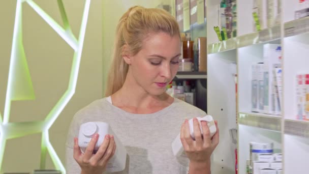 Schöne Frau schaut verwirrt und wählt zwischen zwei Produkten in der Apotheke — Stockvideo