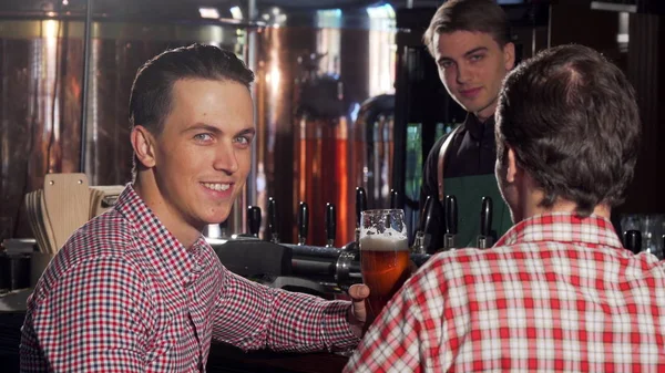 Handsome man clinking glasses with his friend, enjoying drinking beer with friend