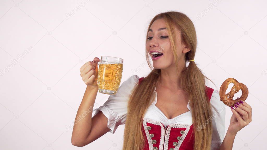 Gorgeous sexy German waitress in dirndl drinking beer, holding delicious pretzel