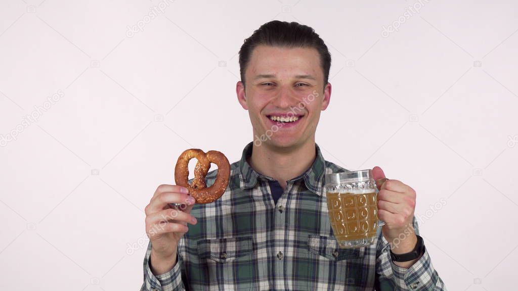 Cheerful young man holding mug of beer, smelling delicious pretzel