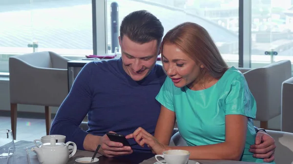 Щаслива любляча пара обіймається, використовуючи смартфон в кафе разом — стокове фото