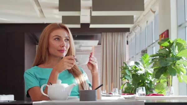 Чудова щаслива жінка виливає чай у чашку, насолоджуючись сніданком у ресторані — стокове фото
