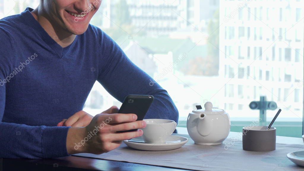 Unrecognizable man smiling, pouring tea, answering emails on his smart phone