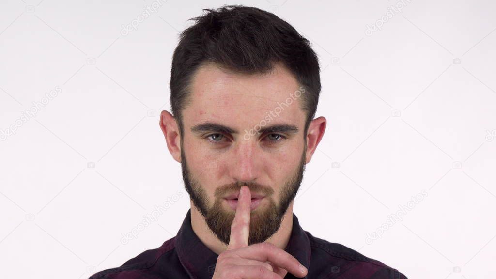 Attractive bearded man shushing to the camera with finger to his lips