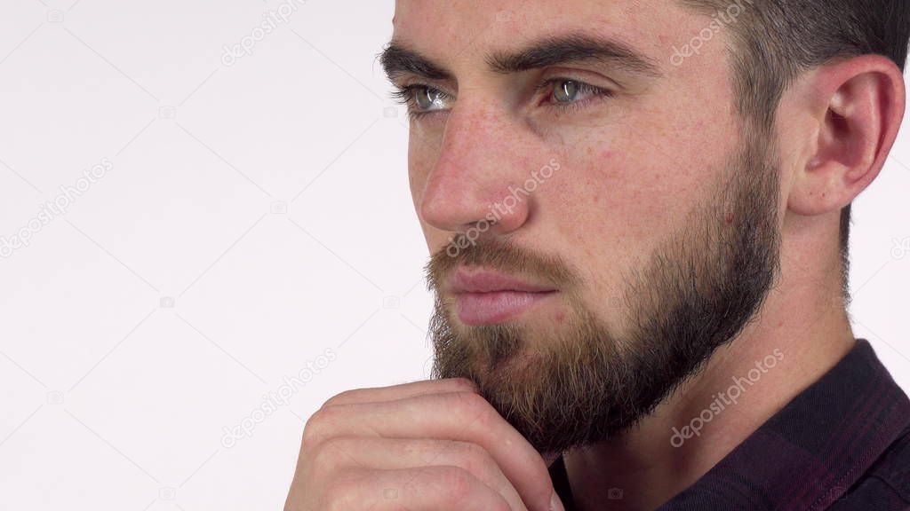 Handsome serious man looking away thoughtfully, rubbing his beard