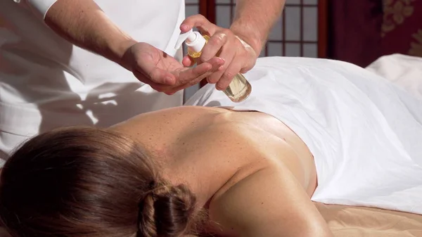 Masajista profesional aplicando aceite a la espalda de su cliente, preparándose para masajear — Foto de Stock