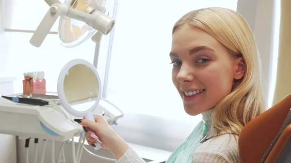 Vista trasera de una paciente femenina mirándose en el espejo en la clínica dental — Foto de Stock