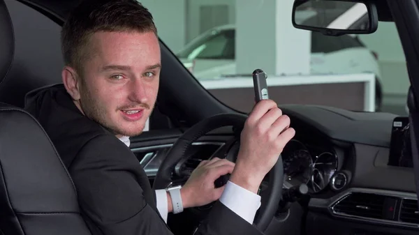 Vousatý podnikatel podal klíč od auta do kamery, sedící v novém automobilu — Stock fotografie