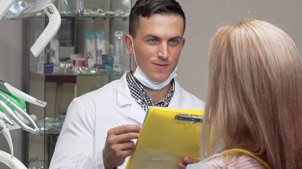 Joven dentista masculino hablando con su paciente femenino, examinando documentos médicos — Foto de Stock