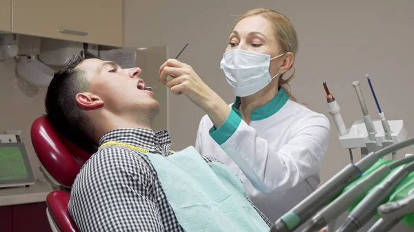 Женщина-дантист осматривает зубы своего пациента, работает в стоматологической клинике — стоковое фото