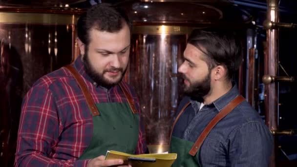 Twee bier makers glimlachen naar de camera, terwijl hij werkte bij hun brouwerij — Stockvideo