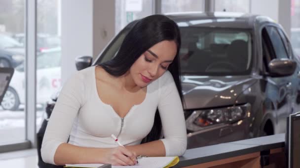 Hermosa mujer sonriendo a la cámara, firmando papeles después de comprar un coche nuevo — Vídeo de stock