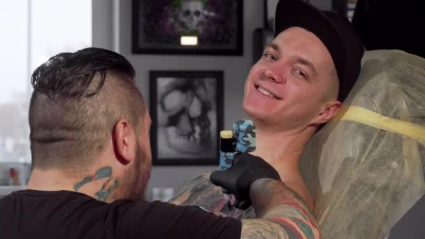 Χαρούμενος νεαρός χαμογελώντας με την κάμερα, ενώ να πάρει τατουάζ — Αρχείο Βίντεο