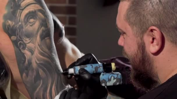 Visão traseira tiro de uma tatuagem fazendo tatuagens no braço do cliente masculino — Vídeo de Stock