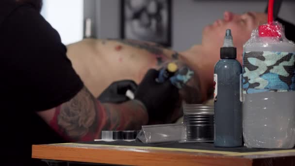 Artista de tatuagem trabalhando em seu estúdio, fazendo uma tatuagem no peito de seu cliente — Vídeo de Stock