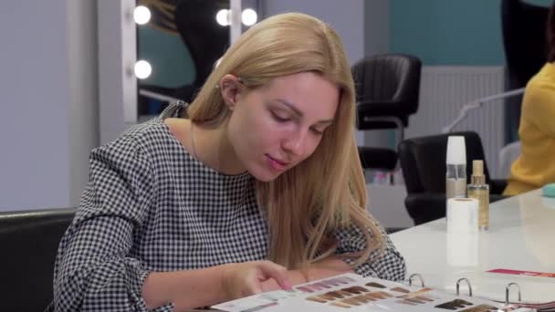 Junge Frau wählt neue Frisur aus Katalog im Friseursalon — Stockvideo