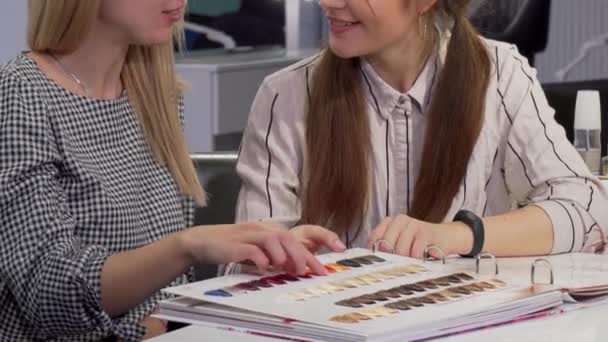 Twee vriendinnen onderzoeken haarkleur kleurstof grafiek bij beauty salon — Stockvideo