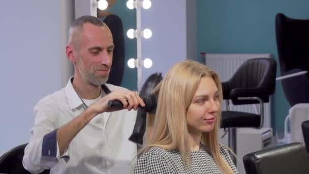 Reife männliche Friseurin föhnen Haare einer weiblichen Kundin im Salon — Stockvideo