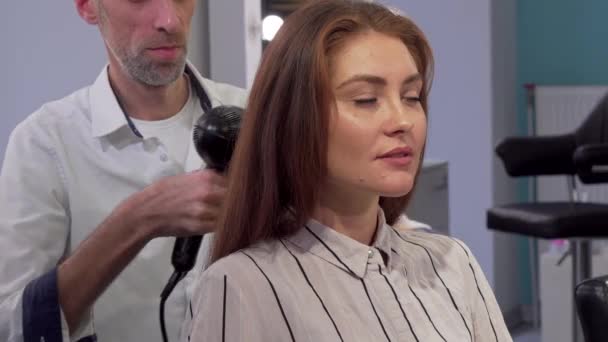 Wunderschöne Frau lächelt in die Kamera, während sie sich die Haare föhnen lässt — Stockvideo