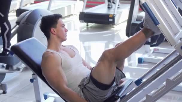 Handsome young ripped male athlete exercising on leg press machine — Stock Video