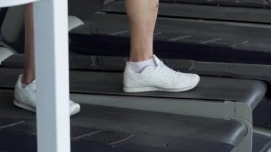 Spor salonunda bir koşu bandı üzerinde yürürken, akıllı telefon kullanarak tanınmayan adam