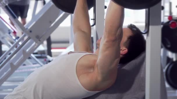 Hombre musculoso guapo haciendo press de banca en el gimnasio — Vídeo de stock