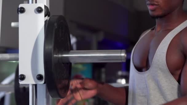 Hombre africano poniendo platos de peso en la barra, haciendo ejercicio en el gimnasio — Vídeos de Stock