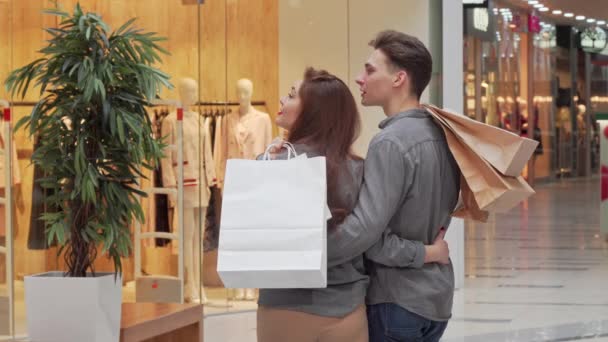 Foto vista traseira de um casal segurando sacos de compras, à procura de uma loja no shopping — Vídeo de Stock