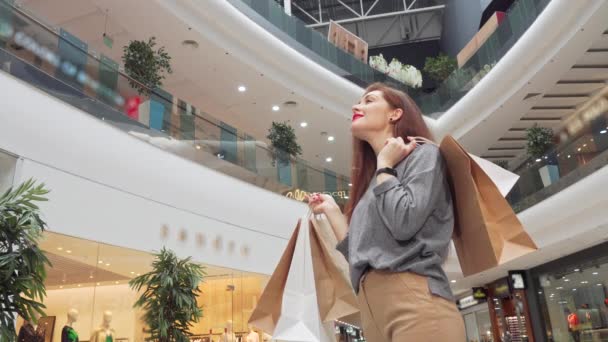 低角度拍摄的一个快乐的女人与购物袋环顾商场 — 图库视频影像