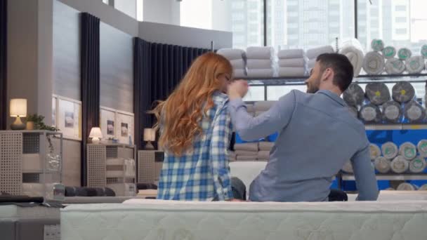 Zadní pohled na pár objetí, sedící na nové posteli v obchodě s nábytkem — Stock video