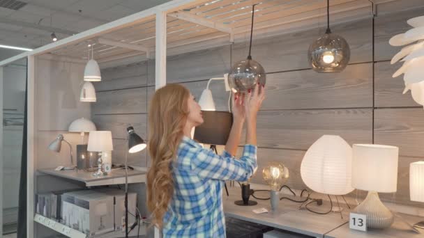 Vista trasera de un cliente femenino eligiendo lámparas en la tienda de muebles — Vídeos de Stock